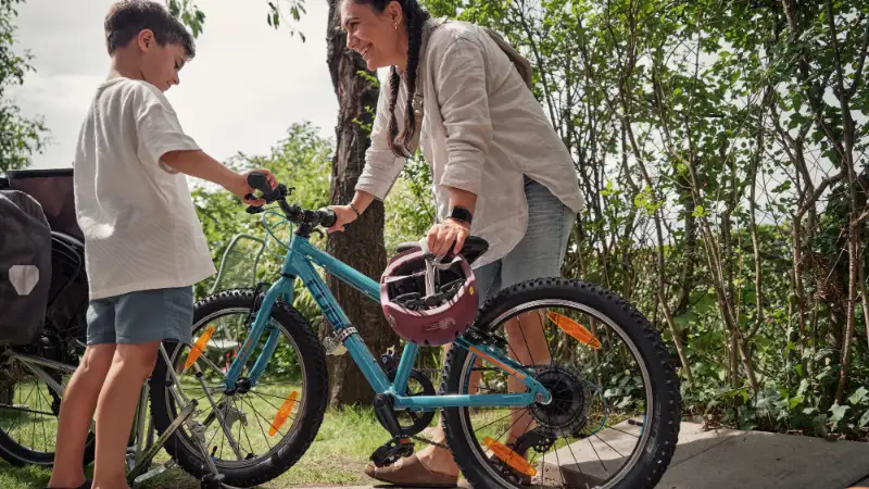 Frau und Junge stehen neben blauem Kinderfahrrad, das per Follow-Me angehängt ist